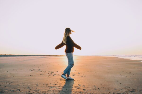Vrouw staat met armen wijd in de zon op een zandvlakte en ervaart rust door hypnotherapie bij angst en paniek.